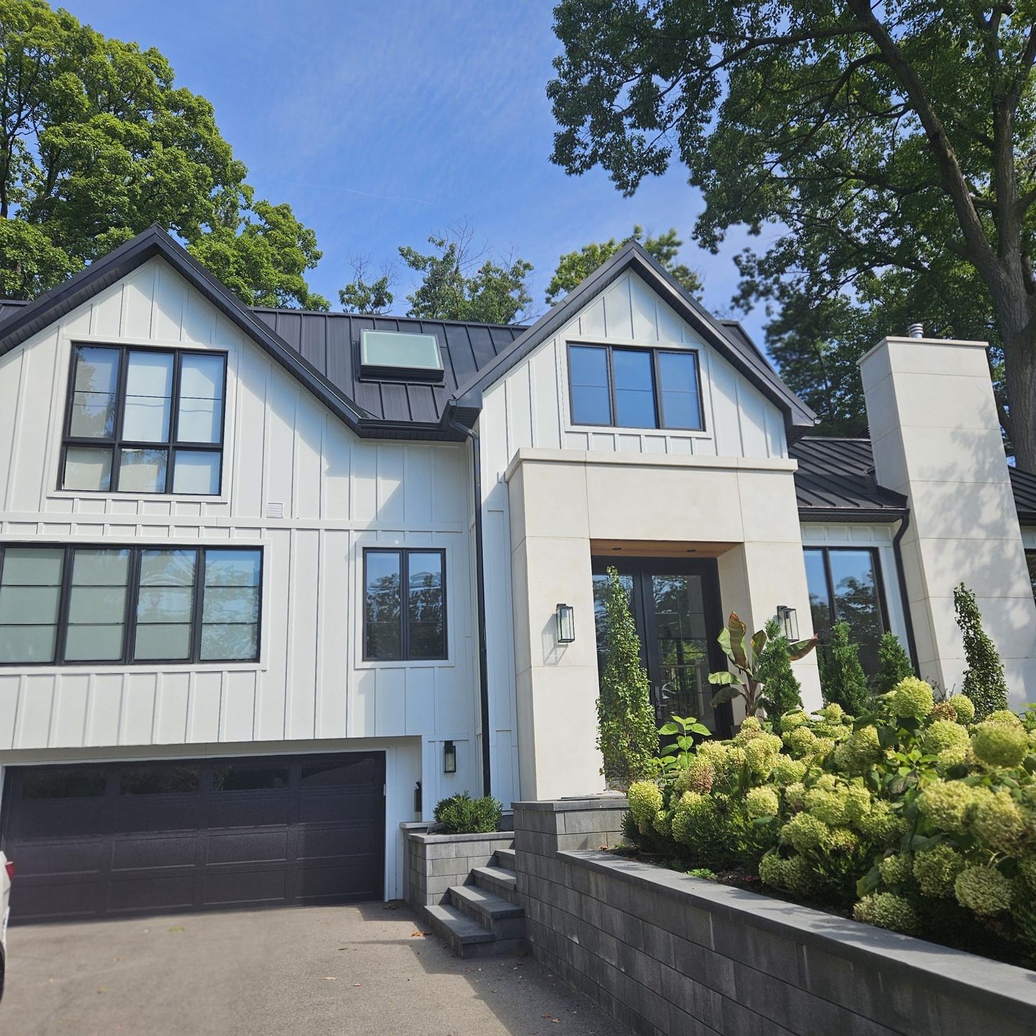 Front exterior of the Brackencrest custom home by Danclair Construction, white board and batten facade with black standing seam metal roof and stone entry