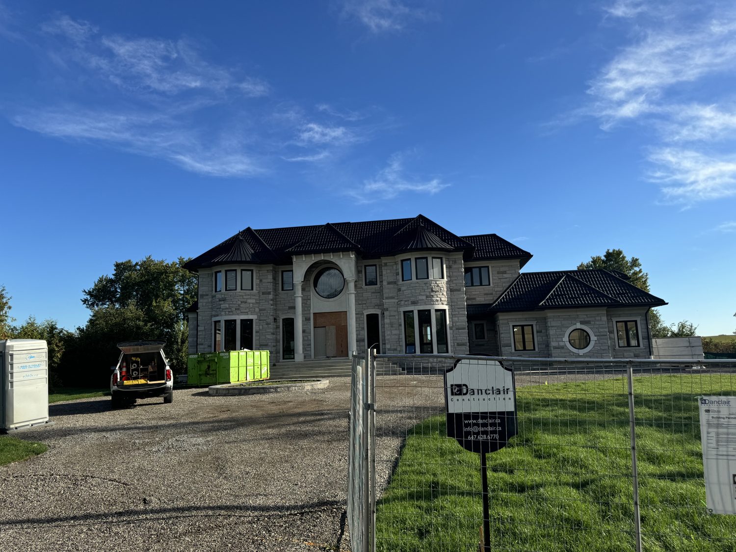 Front elevation of the Eighth Line custom home by Danclair Construction, stone facade with black hip roof and round feature window